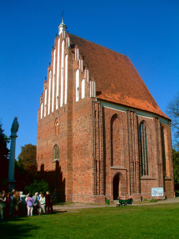 Widok na niewielką, jednonawową gotycką świątynię z czerwonej cegły z wysokim szczytem.
