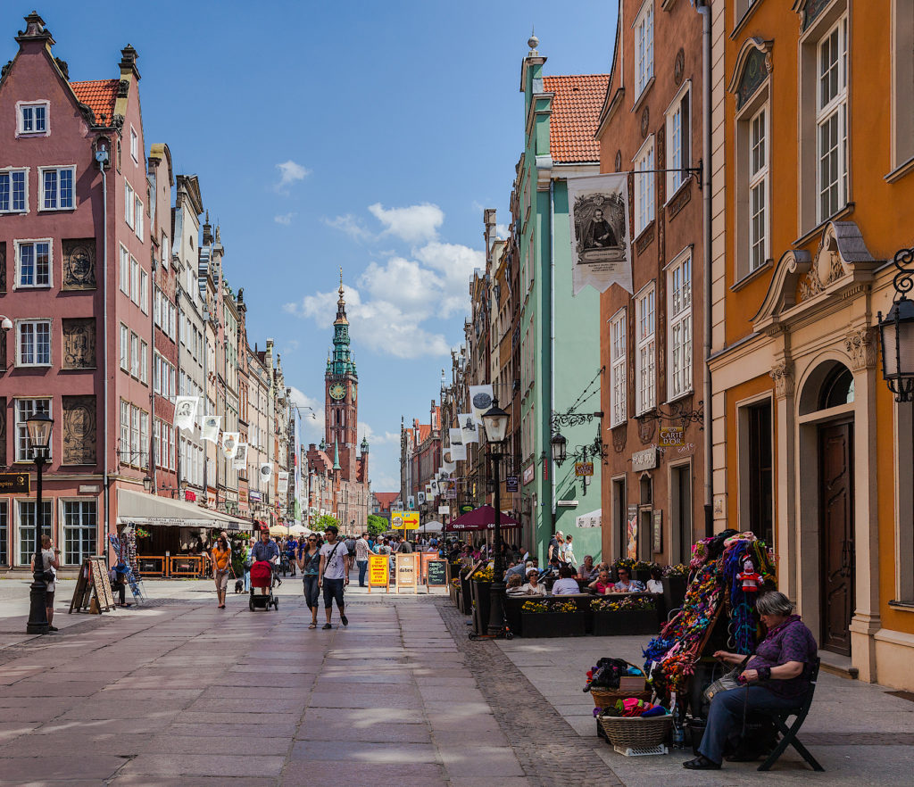 Widok na ulicę Długą w Gdańsku. Po obu stronach rząd kamieni, w oddali widoczny gotycki ratusz z wieżą.