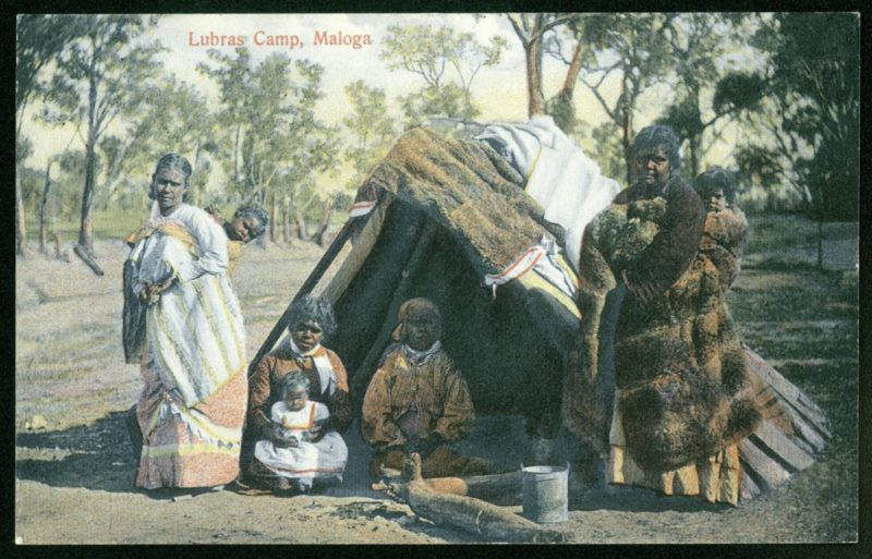 Aborygenki w strojach europejskich, ok 1900 r. Widoczne w podpisie słowo „Lubras” to obraźliwe XIX-wieczne określenie używane w Australii w odniesieniu do aborygeńskich kobiet (fot. domena publiczna) Kolorowe zdjęcie przedstawiające grupę ciemnoskórych kobiet na tle buszu. Dwie z nich stoją po dwóch stronach szałasu, przed którym siedzą dwie kolejne. Trzy z nich trzymają w rękach małe dzieci. Wszystkie noszą europejskie ubrania, a kobieta po prawej dodatkowo ma na sobie brązowe futro zwierzęce.