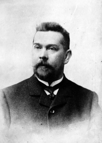 Czarno-biały portret (popiersie) mężczyzny mającego ok. 35 lat, z krótką brodą i wąsami.