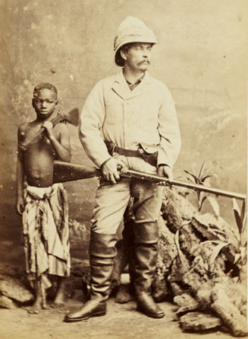 Henry Morton Stanley ze strzelbą i w hełmie korkowym. Obok stoi Ndugu M’Hali (Kalulu) – niewolnik uwolniony przez Stanleya, jego służący i towarzysz (fot. London Stereoscopic & Photographic Company, Smithsonian Institution Libraries, nr SIL28-277-01, domena publiczna)