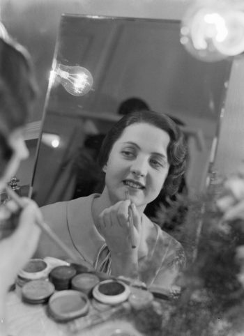 Jadwiga Smosarska przed lustrem w garderobie teatru. Aktorka poprawia zarys ust kredką.