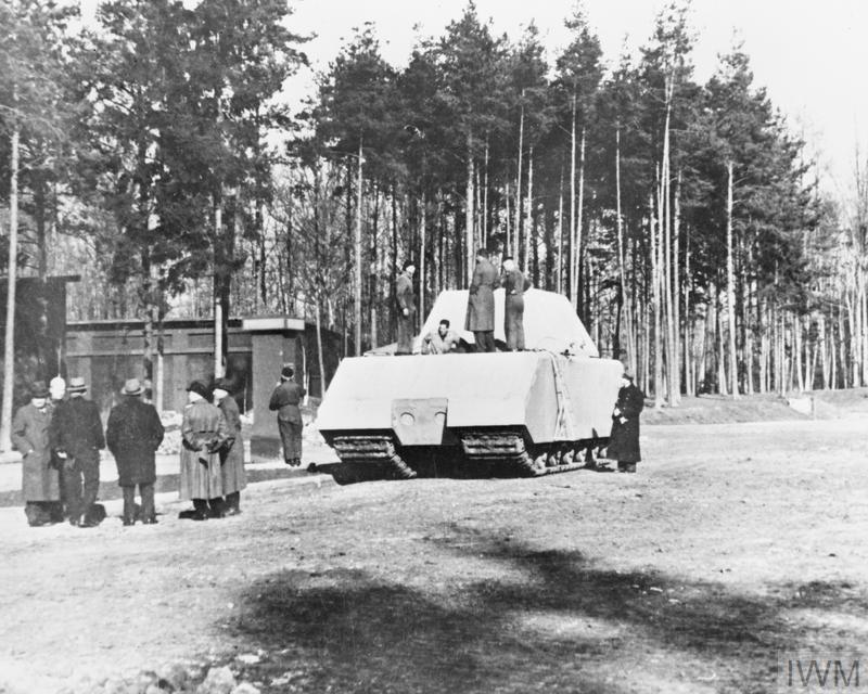 Maus w czasie testów poligonowych (fot. ze zbiorów Imperial War Museum, nr STT 9485, IWM Non Commercial Licence) Czołg Maus – biały kadłub z wieżą (armata niewidoczna) na leśnej polanie (?). W pobliżu stoi grupka mężczyzn, a na kadłubie kilkoro żołnierzy.
