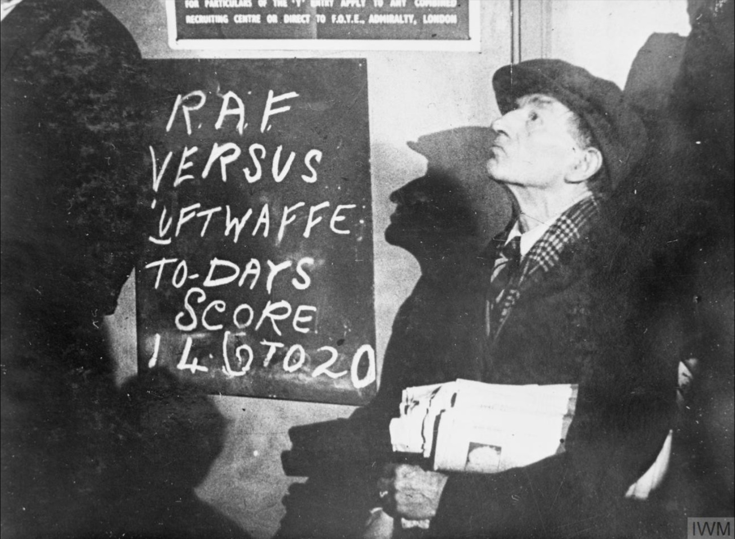 Uliczny sprzedawca gazet obserwuje walkę powietrzną w czasie bitwy o Anglię (fot. Imperial War Museum, sygn. HU 810, IWM Non-Commercial Licence)